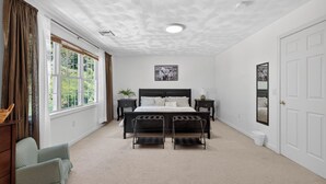 Ein Schlafzimmer mit einem großen Bett, zwei Nachttischen, einem Fenster mit Vorhängen, einer Decke mit Struktur und einer Tür.