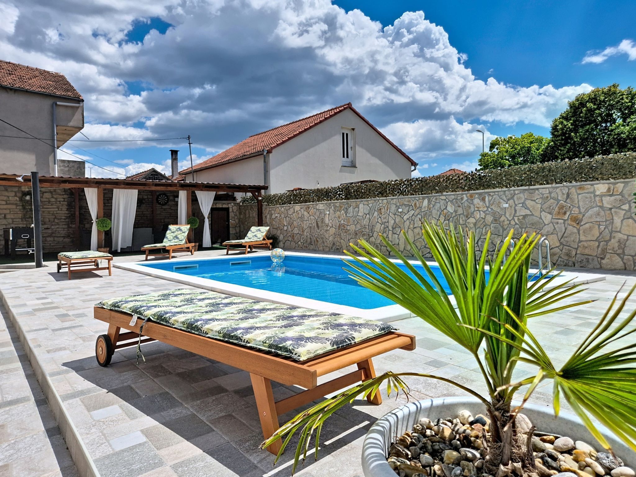 A swimming pool with lounge chairs, a palm plant, and a stone wall.