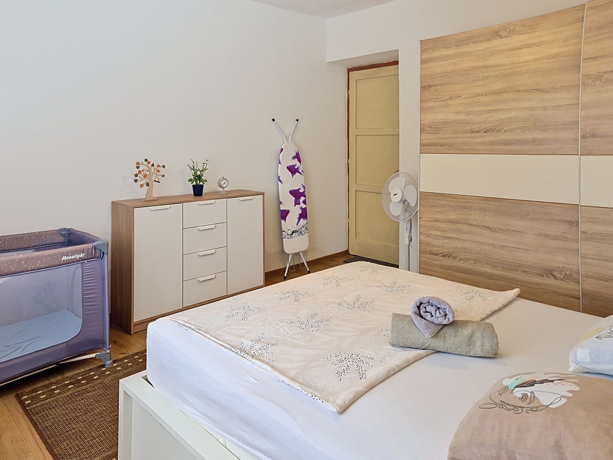 A bedroom with a bed, bedside table, dresser, and a small desk with a chair.