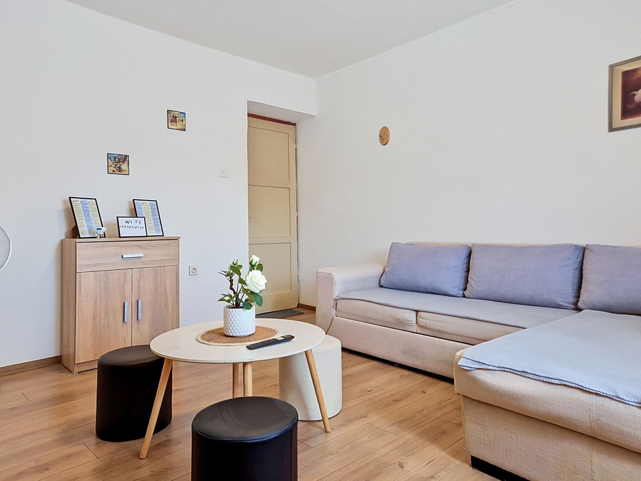 A modern living room with a sofa, a small round table with a vase, a cabinet, and a door.