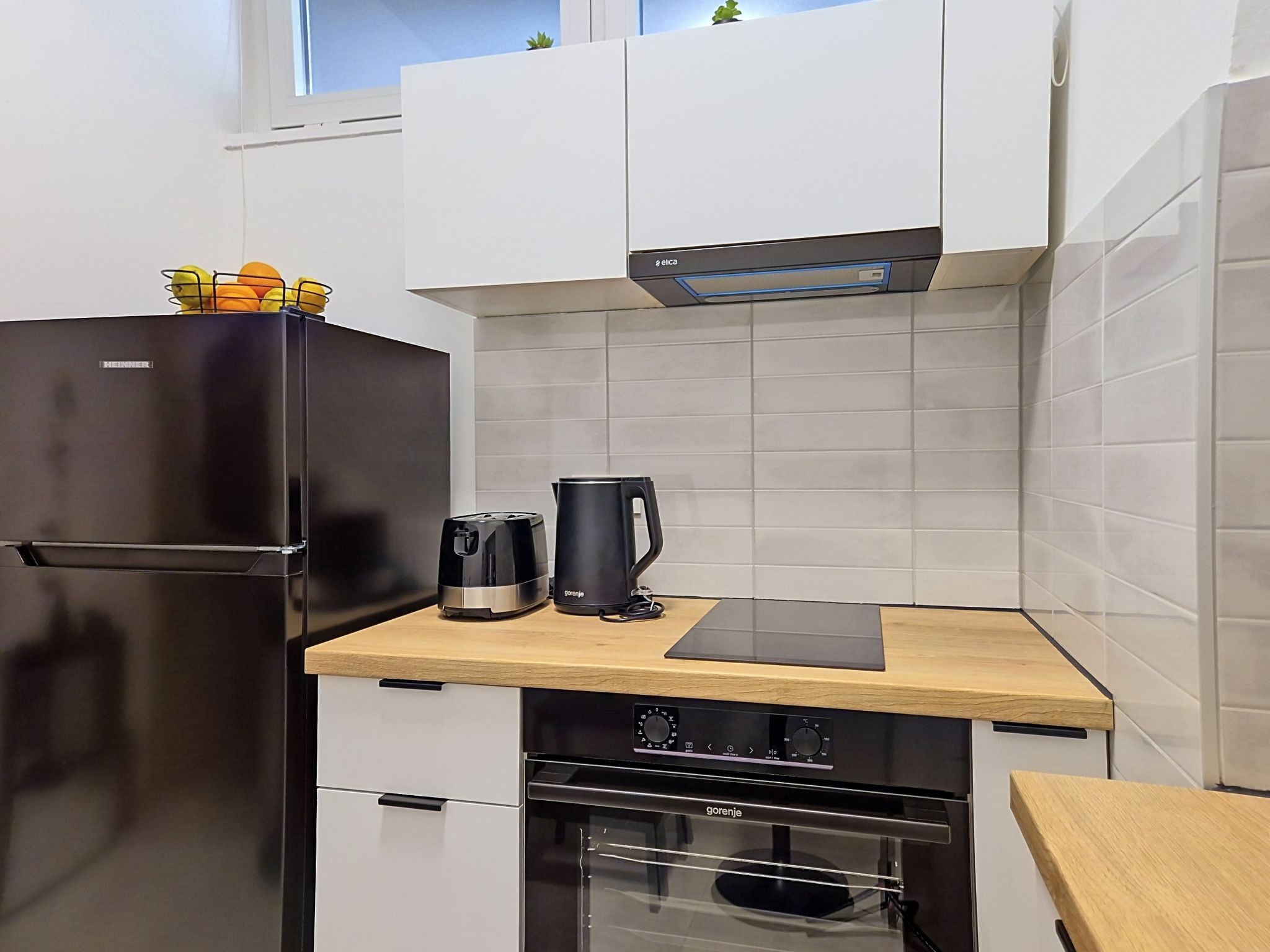 Una cocina compacta con un refrigerador negro, una cafetera y una estufa.