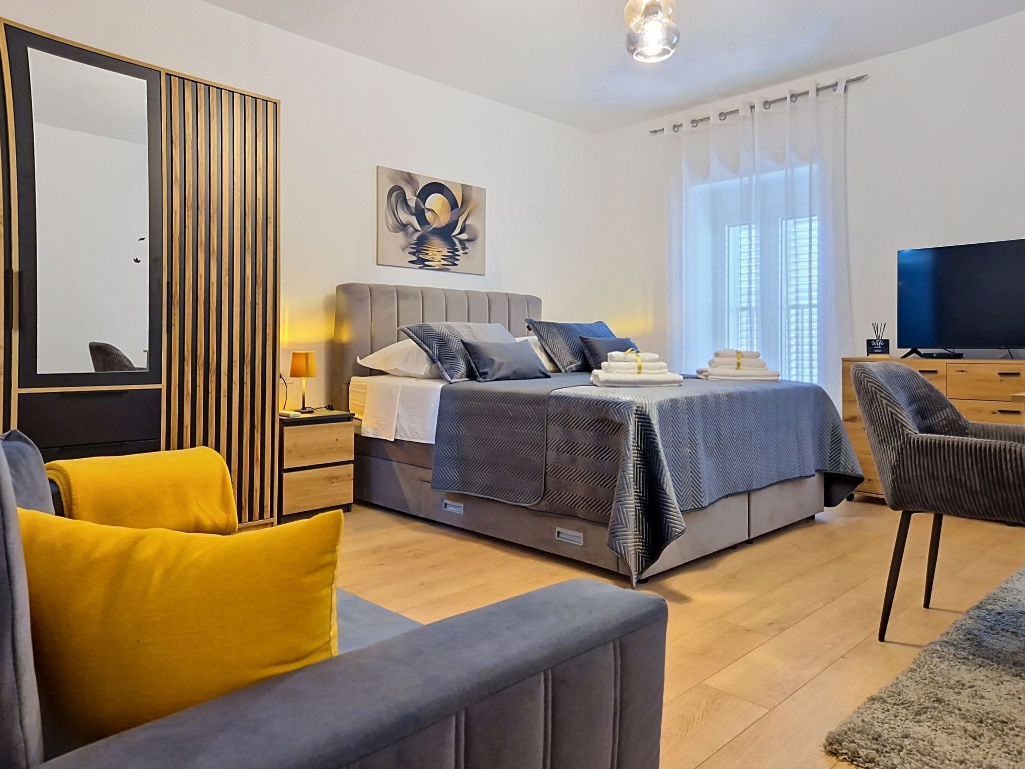 A modern bedroom with a bed, bedside tables, a TV, and a sofa.