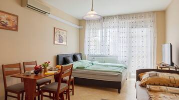 Une chambre à coucher avec un lit, un bureau avec des chaises, une télévision et une fenêtre avec des rideaux.