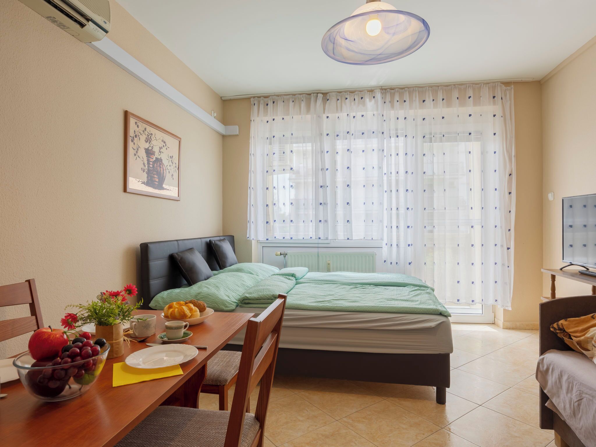 A room with a bed, a desk with a chair, a television, and a window with curtains.