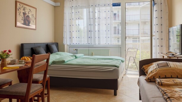 Een slaapkamer met een bed, een bureau met stoel, een televisie en een raam met gordijnen.