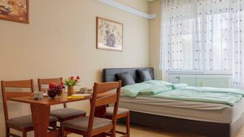 Een slaapkamer met een bed, een eettafel met stoelen, een raam met gordijnen en een radiator.