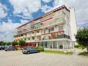 Ein mehrstöckiges Wohngebäude mit Balkonen, einem überdachten Eingang und einem Parkplatz.