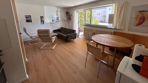 A modern living room with a sofa, a dining table, and a chair. There are framed pictures on the wall, a radiator, and a window with curtains. - Solaria 31 Ferienhaus, Dusche oder Bad, WC 5 1/2- Ferienhaus by Interhome (Davos)