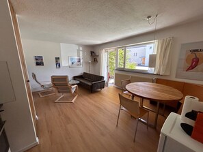 A modern living room with a sofa, a dining table, and a chair. There are framed pictures on the wall, a radiator, and a window with curtains. - Solaria 31 Ferienhaus, Dusche oder Bad, WC 5 1/2- Ferienhaus by Interhome (Davos)