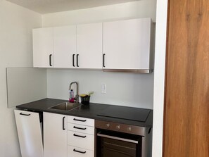 A compact kitchen with white cabinets, a stainless steel sink, a black countertop, and a built-in oven. - Solaria 31 Ferienhaus, Dusche oder Bad, WC 5 1/2- Ferienhaus by Interhome (Davos)