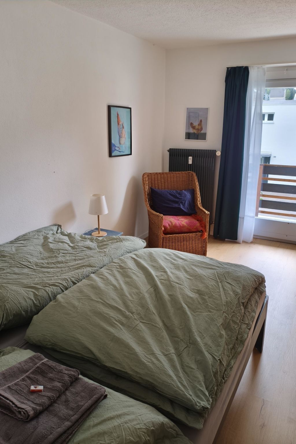 A room with two beds, a chair, a lamp, and a window with curtains.