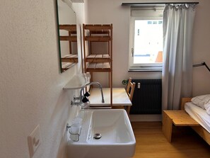 A compact room with a sink, mirror, wooden shelves, a window with curtains, and a bed. - Solaria 31 Ferienhaus, Dusche oder Bad, WC 5 1/2- Ferienhaus by Interhome (Davos)