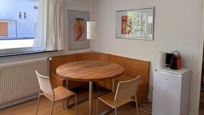 A compact room with a round wooden table, two wicker chairs, a white radiator, a small white fridge, and a window with curtains. - Solaria 31 Ferienhaus, Dusche oder Bad, WC 5 1/2- Ferienhaus by Interhome (Davos)