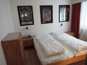 Ein Zimmer mit zwei Betten, einem Holzschrank und drei gerahmten Kunstwerken an der Wand.