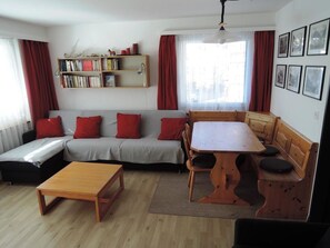 Ein Wohnzimmer mit einer Couch, einem Holztisch, einem Bücherregal und einem Essbereich.