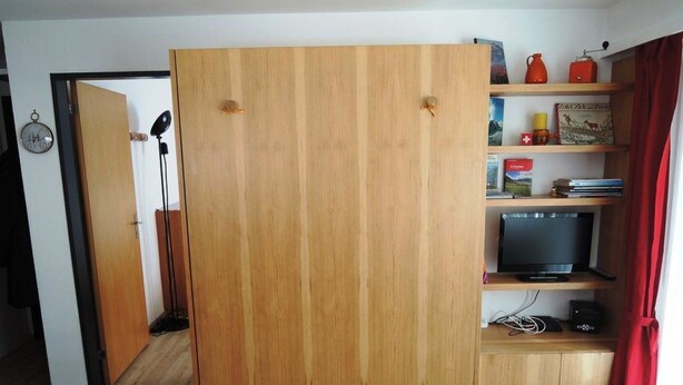 Una stanza con un'armadiatura in legno, una televisione su uno scaffale e una tenda rossa.