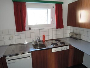 A compact kitchen with a sink, stove, and dishwasher, featuring wooden cabinets and a window with red curtains. - Heimstrasse 1 App 4 Appartement/Fewo, Dusche oder Bad, WC, Balkon by Interhome (Davos)