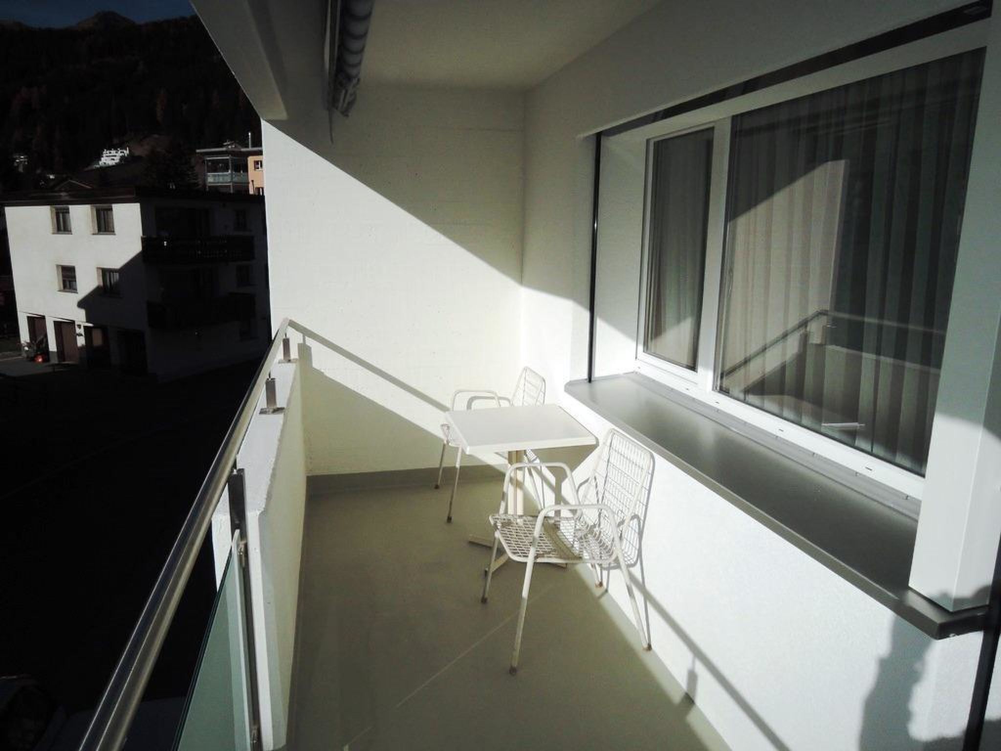 A balcony with a table and chairs, a window, and a view of buildings.