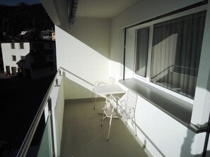 Ein Balkon mit Tisch und Stühlen, ein Fenster und Blick auf Gebäude.