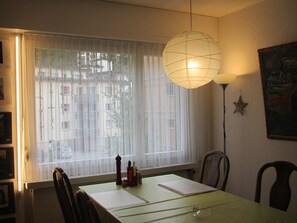 Uma área de refeições com uma mesa, cadeiras, luminária pendente, janela com cortinas leves e um enfeite de estrela na parede.