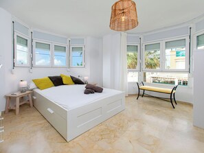 Ein Schlafzimmer mit Bett, Nachttisch, Lampe, Bank und großen Fenstern.