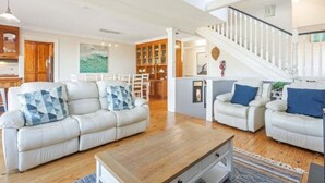 Un vaste espace de vie comprenant un ensemble de canapés, une table basse et un escalier menant à un niveau supérieur.