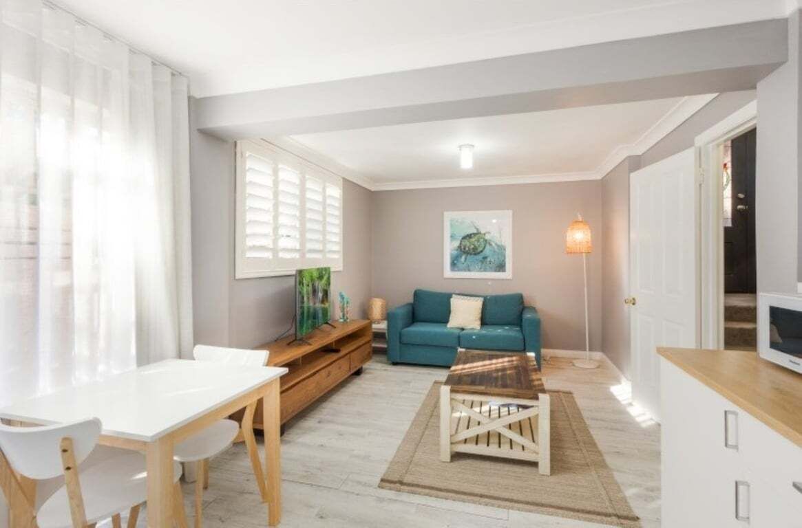 A living room with a white table, teal sofa, and a TV on a wooden stand.