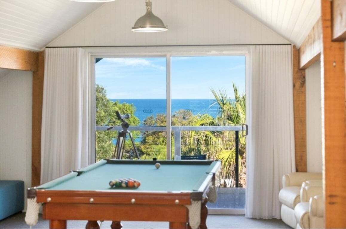 The expansive loft entertainment room includes a premium pool table positioned perfectly against a backdrop of panoramic ocean views.