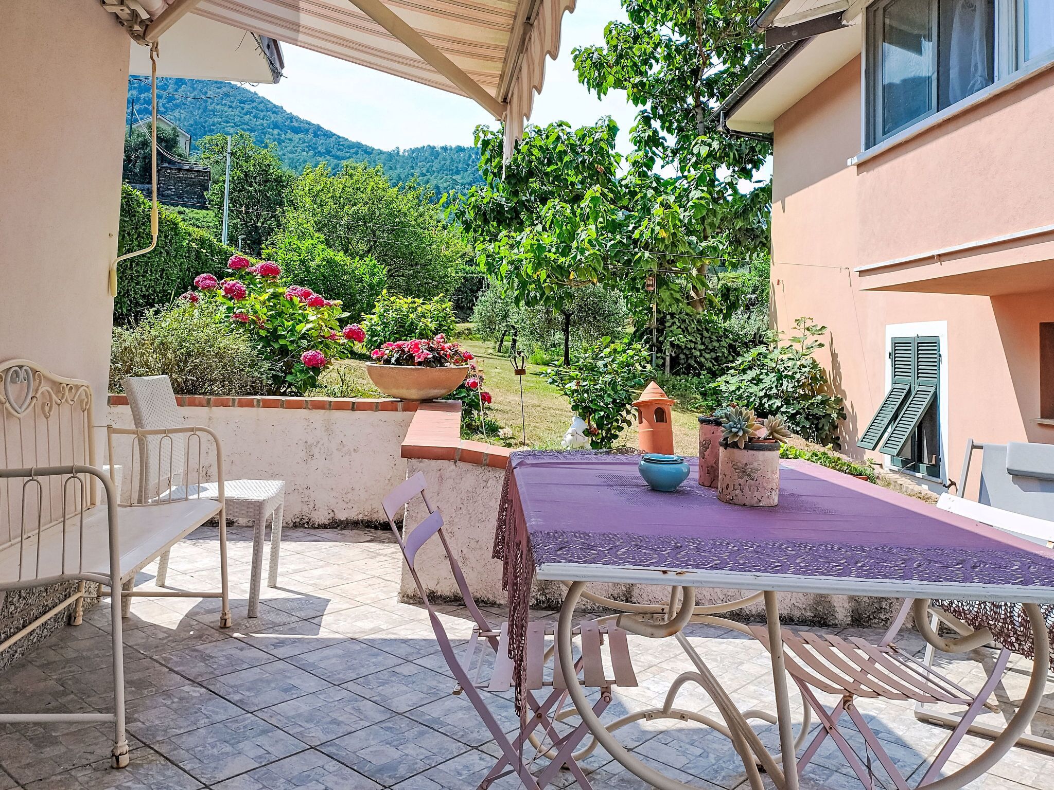 An outdoor patio with a table and chairs, surrounded by potted plants and a view of a mountainous landscape.