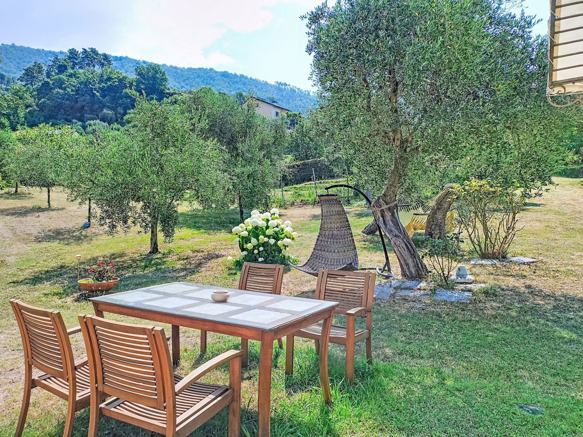 An outdoor dining area with a table and chairs, surrounded by trees and a view of a hillside.