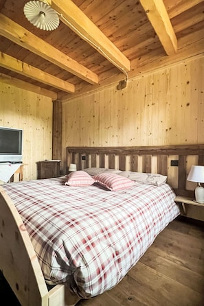 A wooden room with a bed, a nightstand, a lamp, and a ceiling fan.