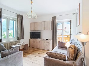 Ein modernes Wohnzimmer mit einer Couch, einem Fernseher, Holzkredenz und Blick auf einen Balkon.