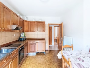 A kitchen with wooden cabinets, a stove, and a sink. There is a dining table with a patterned tablecloth. - Edelweiss by Interhome (Pozza di Fassa)