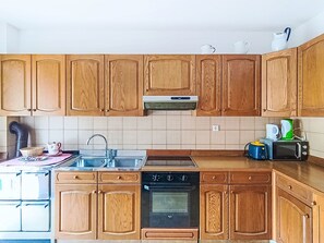 Eine Küche mit Holzschränken, einem Herd, einem Backofen, einer Mikrowelle und einem Spülbecken.