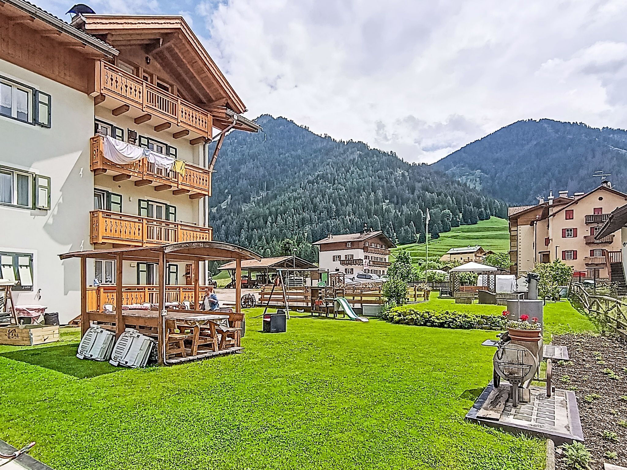 A multi-story building with balconies, a grassy courtyard, and a mountainous backdrop.
