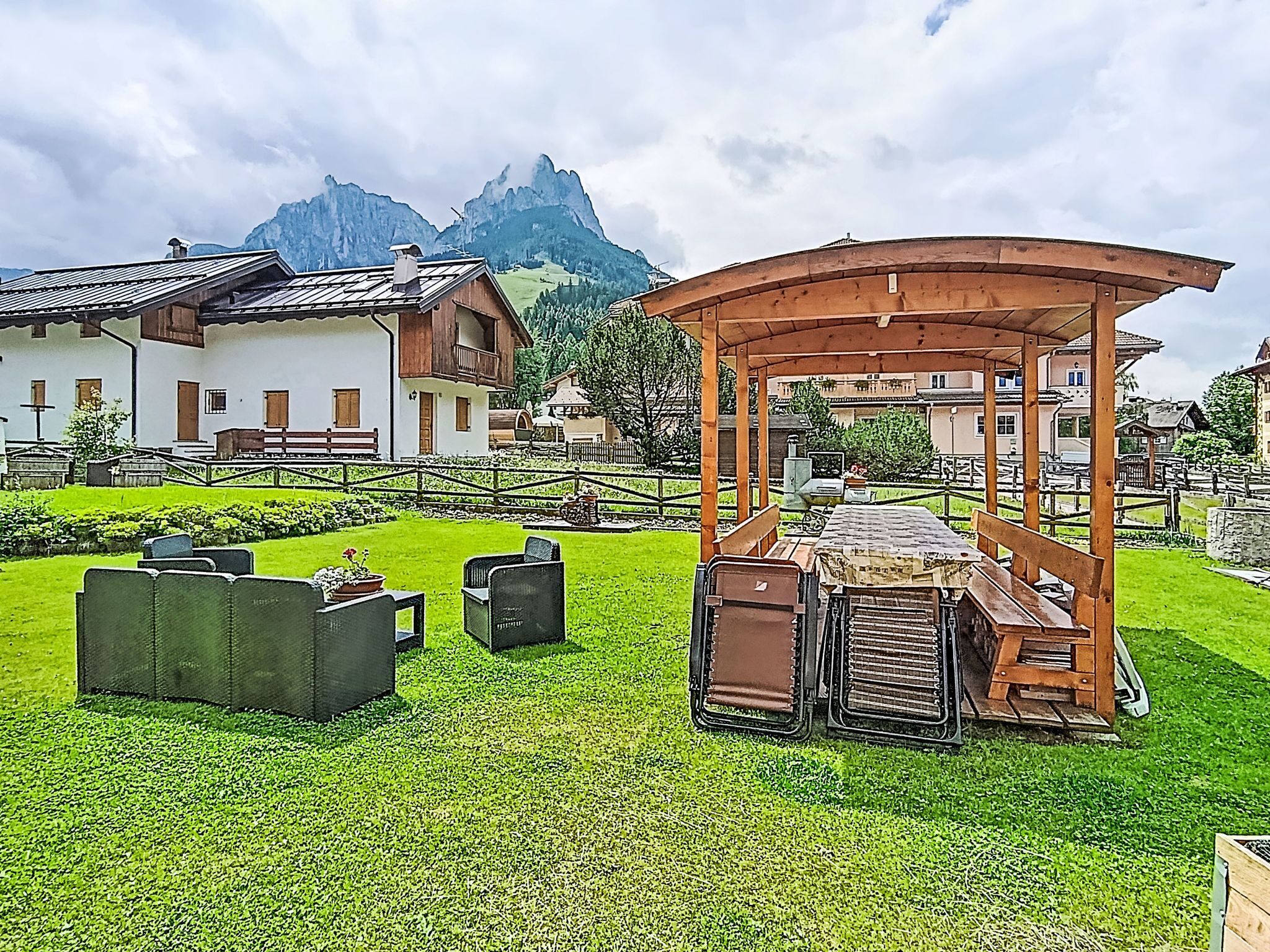 A chalet with a wooden pergola, outdoor seating, and a mountainous backdrop.