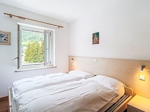 A bedroom with a bed, a window with a view of trees, a wall-mounted light, and a small picture. - Edelweiss by Interhome (Pozza di Fassa)