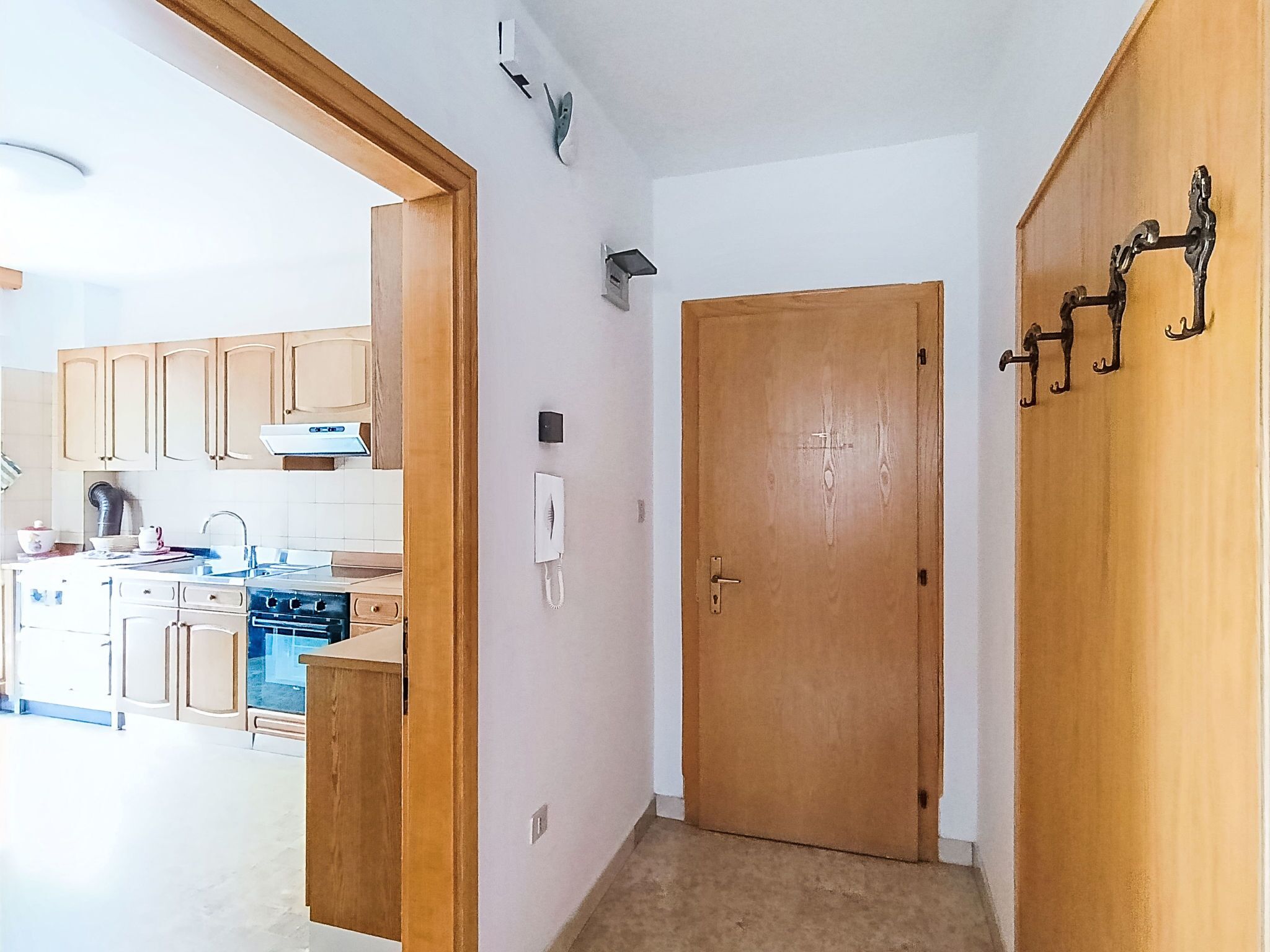 A hallway leading to a kitchen with wooden cabinets, a stove, and a sink.