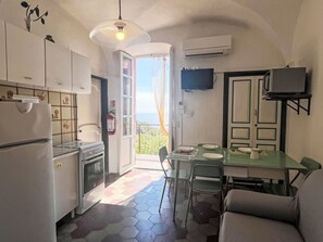 A compact kitchen with a dining area, a TV mounted on the wall, and a view through the open door. - Risorgimento Apartment by Interhome (Cipressa)