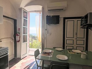 A compact kitchen with a dining area, an open door leading to a balcony, a fire extinguisher, and a mounted television. - Risorgimento Apartment by Interhome (Cipressa)