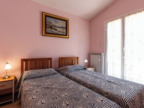 Ein Schlafzimmer mit zwei Betten, einem Nachttisch, einer Lampe, einem Heizkörper und einem Fenster mit Vorhängen.