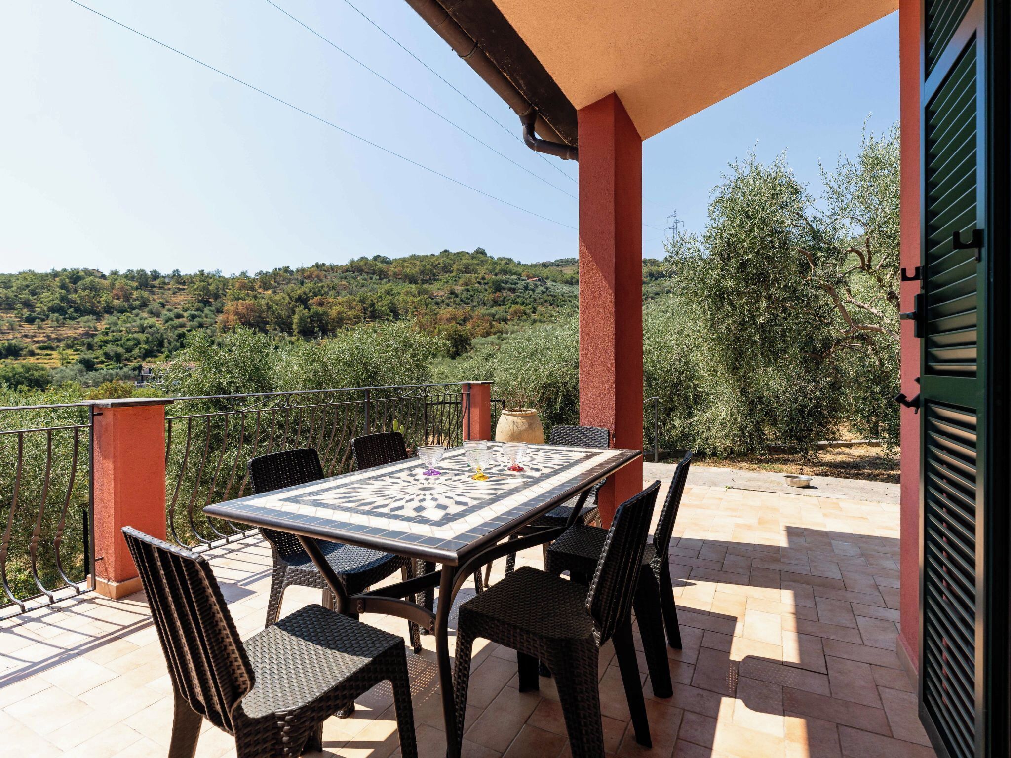 Una terrazza con tavolo e sedie, vista su un paesaggio collinare e un pilastro rosso.