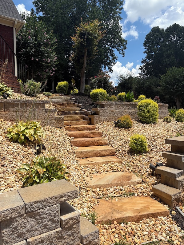 A stone staircase leading up to a building, surrounded by a landscaped garden with various plants and trees.
