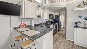 A modern kitchen with a central island, bar stools, and a dining area. - Cast N' Cork Casita - 1 Bedroom Charming Lakefront Cabin (Weatherford)