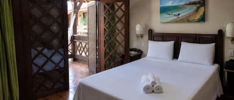 A hotel room with a bed, a painting of a beach, and a view through an open door to an outdoor area.