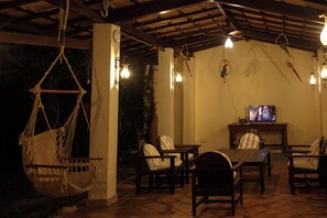 A cozy outdoor seating area with hammocks, chairs, and a television. - Pousada Rosa dos Ventos (Porto Seguro)