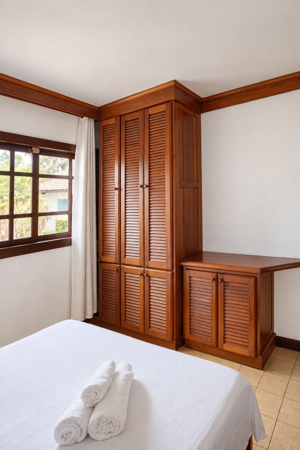 A hotel room with a bed, a wooden wardrobe, and a window with curtains.