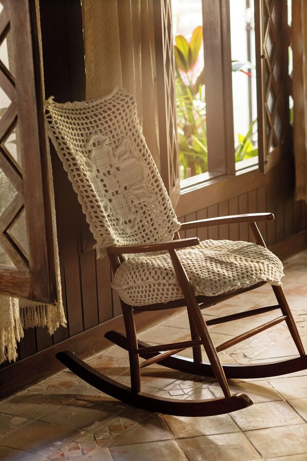 A rocking chair with a crocheted seat and backrest, positioned in a room with wooden walls and a tiled floor.