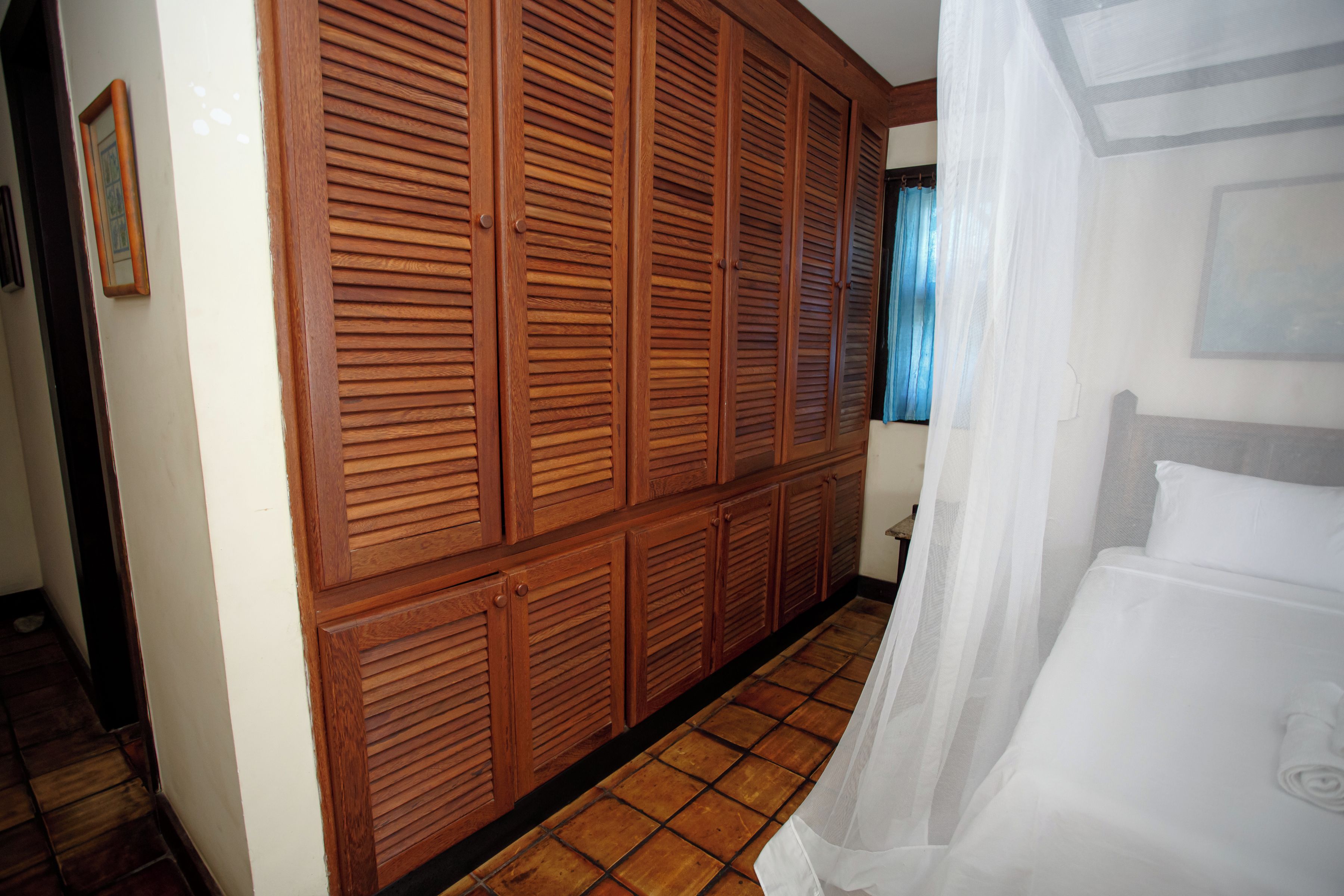 Quarto de hotel com um grande guarda-roupa de madeira, uma cama com roupa de cama branca e um chão em azulejos.