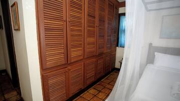 Quarto de hotel com um grande guarda-roupa de madeira, uma cama com roupa de cama branca e um chão em azulejos.